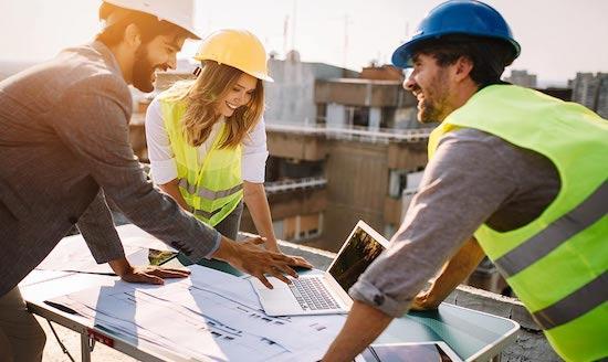 A group of people wearing hard hats and vests looking at a computer
Description automatically generated